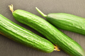 Three green cucumbers, close-up, on a slate board, top view.