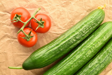 Several green cucumbers and red ripe, cocktail tomatoes on a twig, close-up, on craft paper, top view.