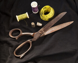 Sewing vintage scissor, measure ruler, thread roll lines and thimble on black textile background - sewing equipment with space to text
