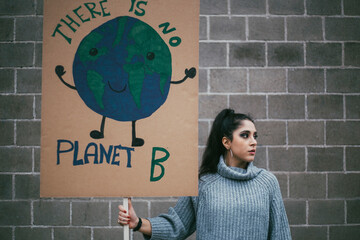 Female activist looking away while holding planet earth poster against wall