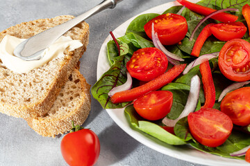 Vegetarian salad of cherry tomatoes, spinach, red onions and bell peppers with butter. On a gray background.