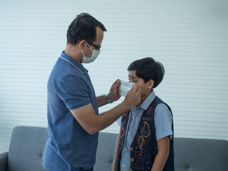 Indian dad helping son putting medical mask before going outside the house. Lifestyles during outbreak of Covid-19 or Coronavirus.