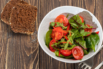 Vegetarian salad of cherry tomatoes, spinach, red onions and bell peppers with butter. On a wooden background.