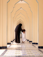 Rear view of Muslilm mother in black traditional and hijab with young boy walking along the...