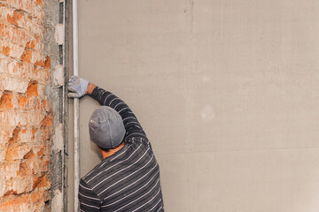The final stage of plastering the walls. A worker levels the plaster with a leveler.
