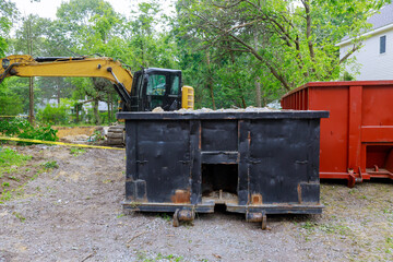 Under construction with excavator bucket on construction trash dumpsters in an metal container,...