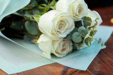 A bouquet of white roses in paper packaging lies on a wooden table.