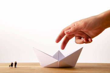 a man is about to pick up an origami paper boat while several miniature figures watch him