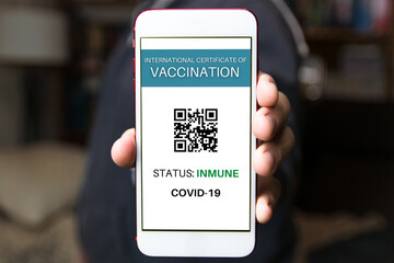 Close-up of a man holding smartphone with the Covid-19 vaccination certificate.