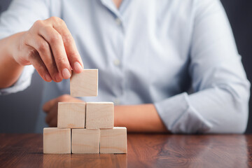 Hand holding a blank wooden block while sitting on a chair. Close-up photo. Space for text