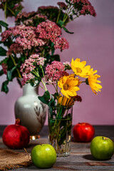Bouquet of flowers in a vase next to apples and pomegranate on a wooden table