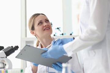 Assistant giving woman chemist clipboard with documents in lab