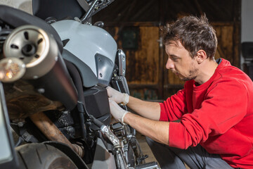 Fototapeta na wymiar Young man repairing or preparing a motorbike for a new season after winter time, basic motorcycle maintenance