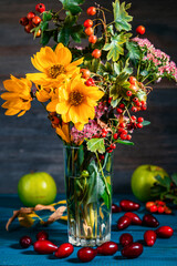 Bouquet of flowers in a vase next to apples and pomegranate on a wooden table