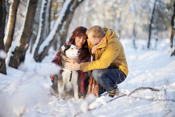 Fototapeta na wymiar Couple smiling and having fun in winter park with their husky dog