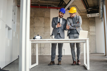 Businessman showing architect how he imagined building on the phone. Construction site.