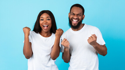 Portrait of happy black couple celebrating win with raised fists