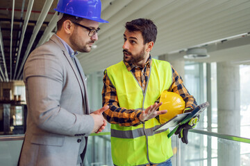 Construction worker holding tablet and explaining his supervisor how works are going. Building in...