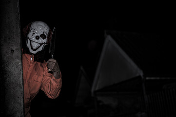 Asian handsome man wear clown mask with weapon at the night scene,Halloween festival concept,Horror scary photo of a killer in orange cloth