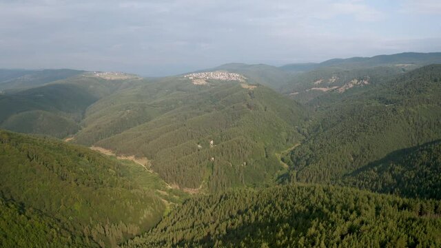 Drone flight over green mountain slopes and a small villages nestled in them, the Rhodopes in Bulgaria