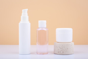 Set of cosmetic bottles with face cream, lotion and lip balm on white table against beige background