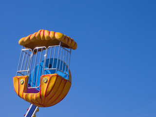 Blue-yellow booth of a children's Ferris wheel against the blue sky.