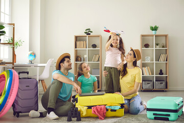 Happy family watching one of excited little daughter playing with toy plane sitting on floor with...