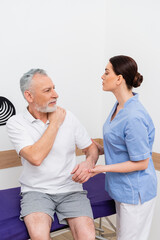 Obraz premium mature man touching shoulder during consultation with rehabilitologist