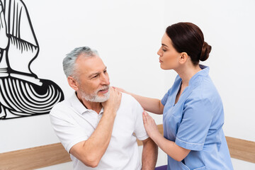 brunette rehabilitologist examining mature man in hospital