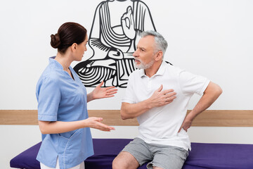 mature man touching chest during consultation with rehabilitologist in hospital
