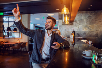 A kind businessman sits at a bar asking for a check. He calls the waiter with one hand while...