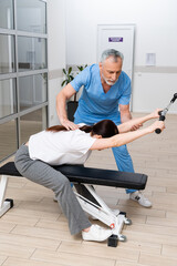 Naklejka na ściany i meble mature physiotherapist helping woman working out in rehabilitation center
