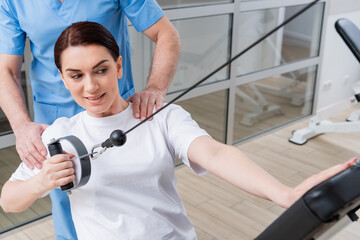 trainer assisting woman working on pull cable exercising machine