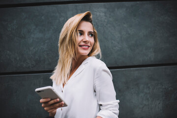 Happy young female standing with smartphone and looking over shoulder