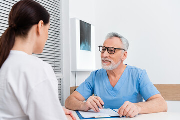 smiling traumatologist talking to brunette woman on blurred foreground