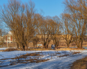 On a sunny day in March, a man and a woman walk in the distance in a city park
