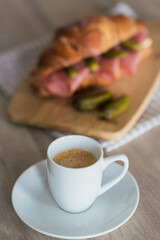 breakfast of coffee and croissant sandwich stuffed with salami and cornichons
