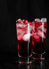 Alcoholic cocktail with red currant and ice cubes in shots on a black background