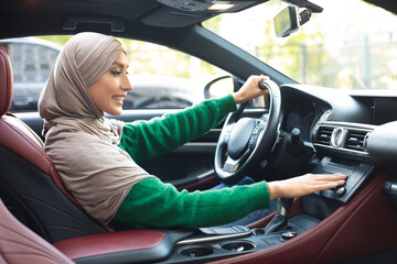 Cheerful muslim woman driving car, turning on music