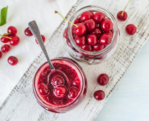 Cherry jam with fresh cherries on a wooden background. Top view