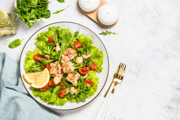 Green salad with baked fish at white table.