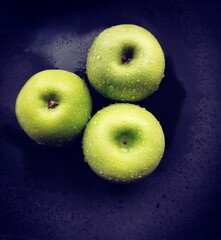 Three Granny Smith apples in water on a black background.