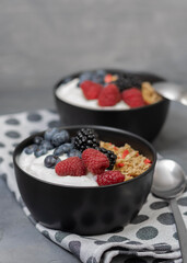 Muesli with yougurt and fresh berries in black bowl on dark gray background.