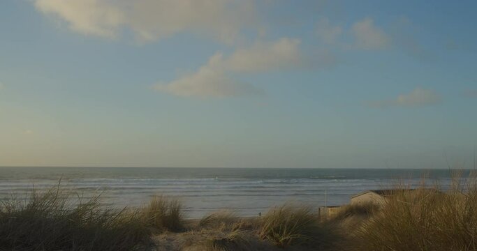 A house behind dunes on windy coast, Perran Sands Beach, golden light