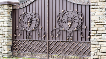 brown metal gate with a forged pattern and a brick fence on the sidewalk on the street.
