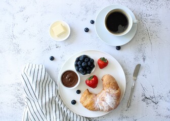Breakfast in French style: croissant, butter, coffee with milk, berries on a light background, top view. Traditional French breakfast with pastries, aromatic espresso and berries, copy space.