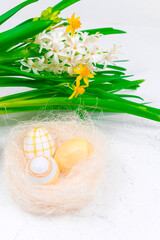 Spring, Easter concept. Yellow Easter eggs in a nest next to a bouquet of daffodils on a white...