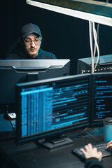 Middle aged Hackers with curly long hair in a sweatshirt, baseball cap and glasses making...