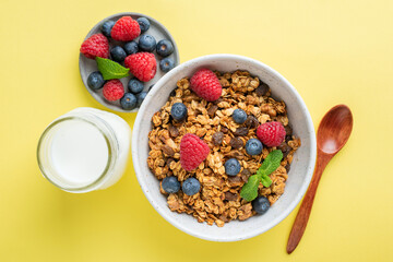 Granola with summer berries and bottle of milk on yellow background. Healthy breakfast cereals food