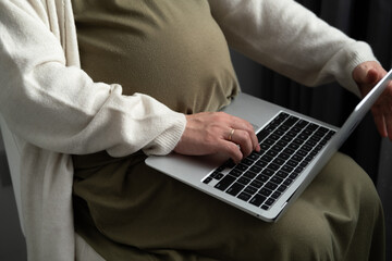 Attractive pregnant young lady working remotely online from home. Close up woman hands on laptop with big belly advanced pregnancy.